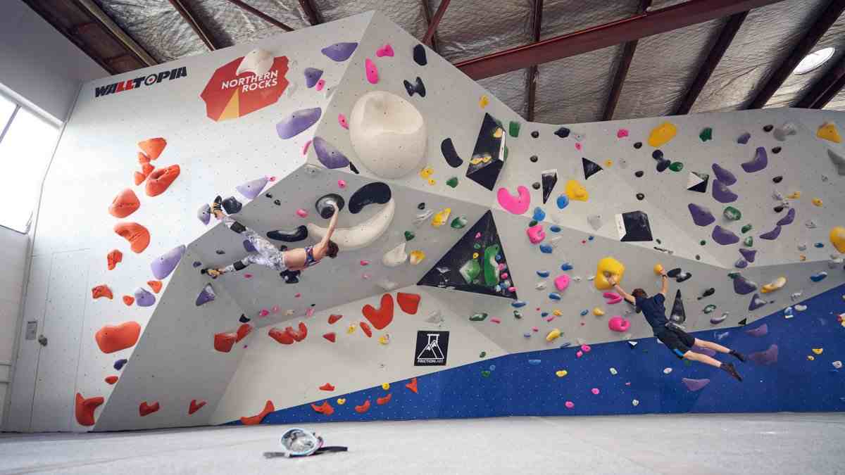 Two boulderers climbing on a colourful overhanging indoor wall.