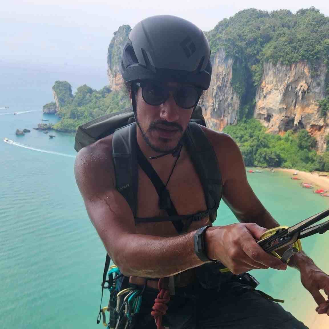 Shirtless climber wearing helmet at belay with ocean in background