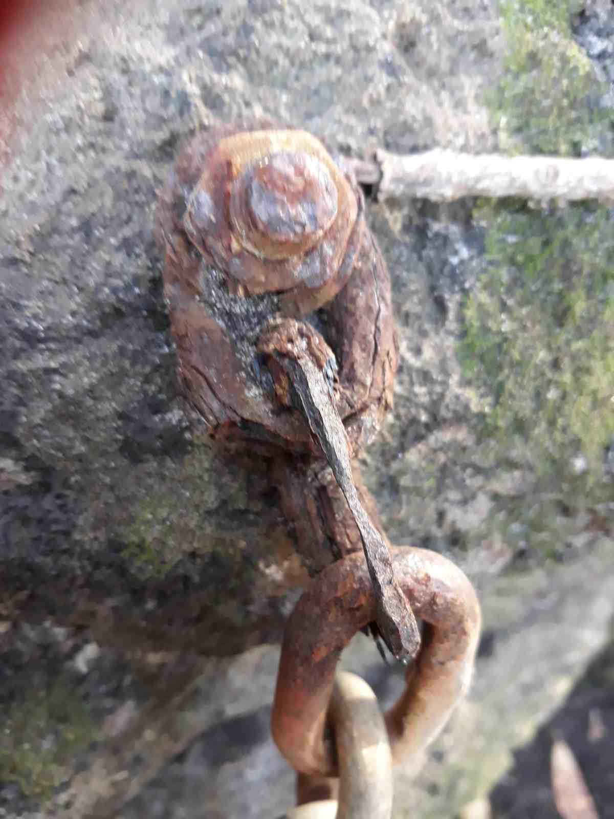 A very rusty chain link climbing anchor bolt on grey rock