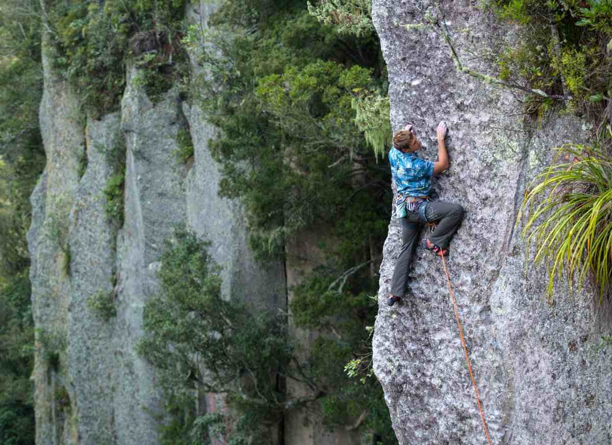 Climber in glue hawaiian white climbs a pocketed face against a bush background