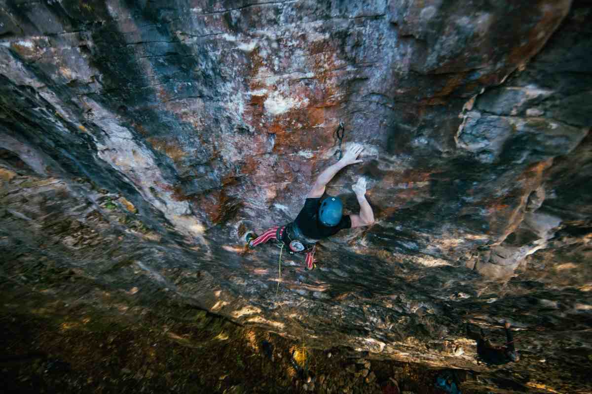 Climber in black shirt and striped tights on shady limestone cliff, seen from above