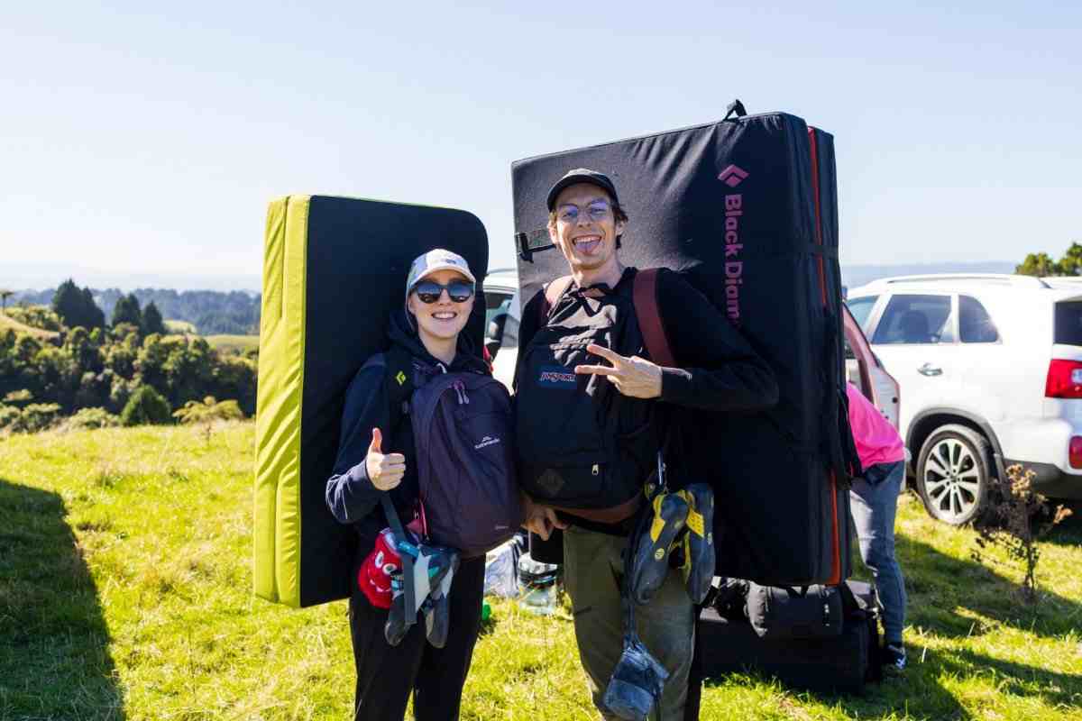 Rock climbers make hand gestures with boulder mats on their backs.