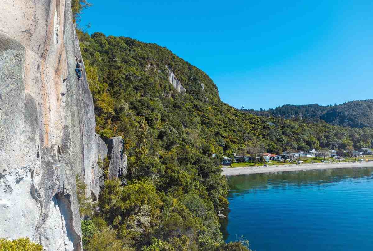 Climber on rockface at Whekenui wall with Whanganui Bay in the background.