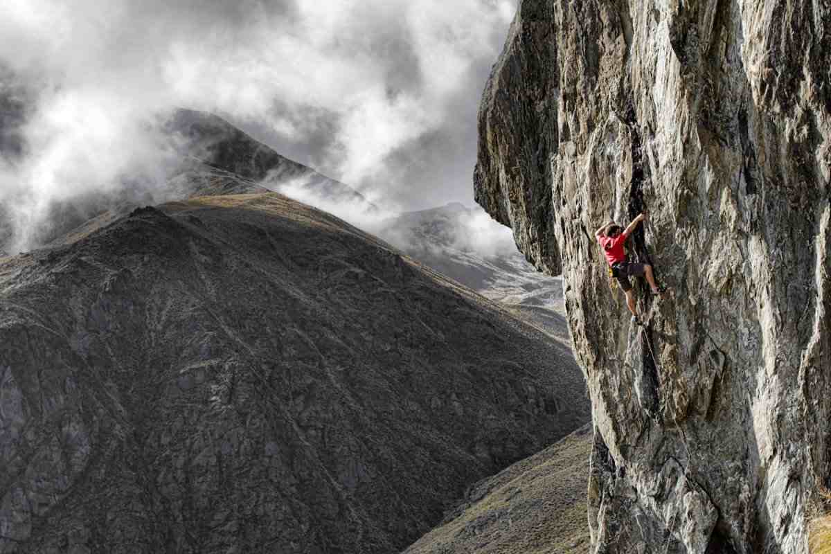 Climber in red shirt high on a rock face in the Remarkables with misty background