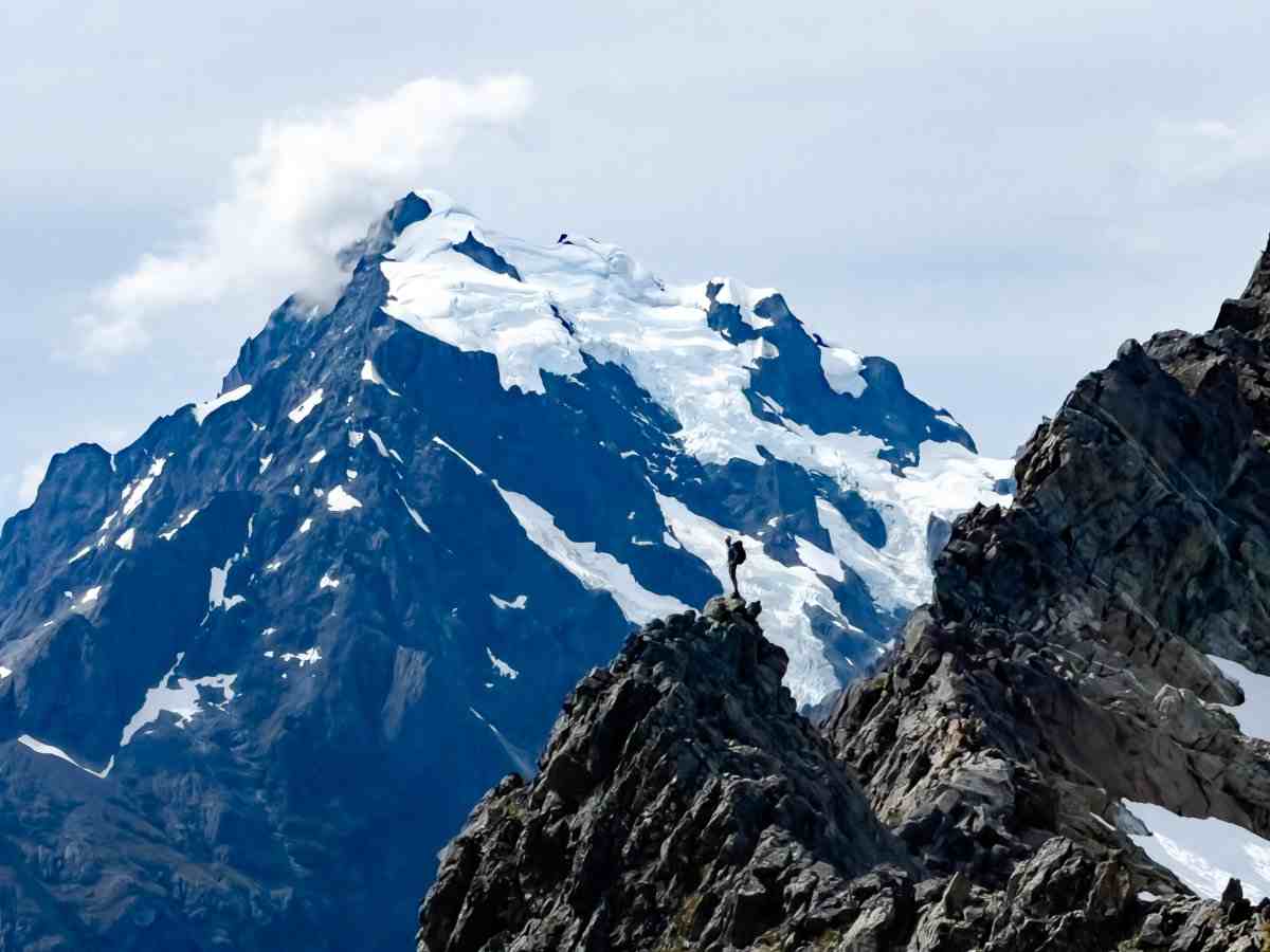 Snowcapped Mt Tutoko in the Darrans with a climber standing on a rocky outcrop in the foreground