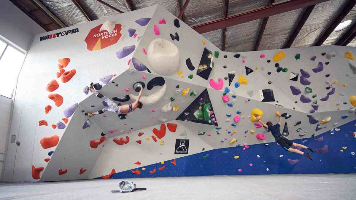 Two boulderers climbing on a colourful overhanging indoor wall.