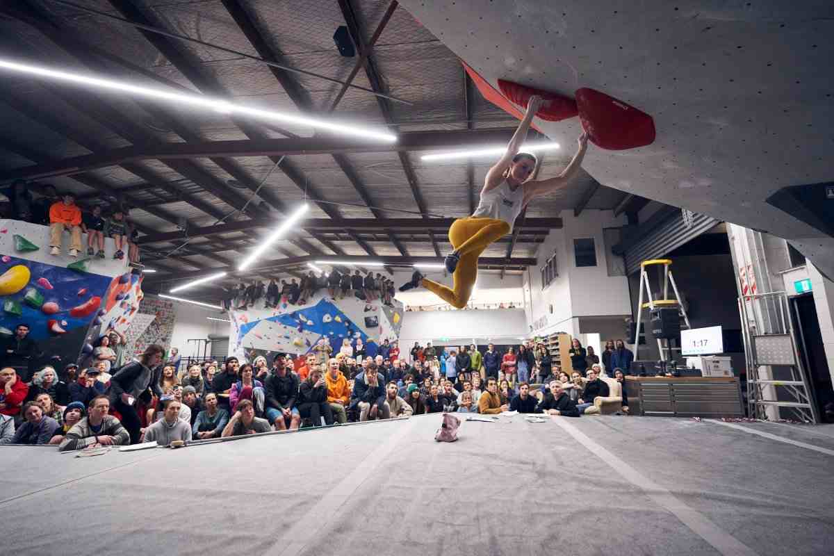 Boulderer with feet in the air in the indoor NIBS competition watched by a crowd.