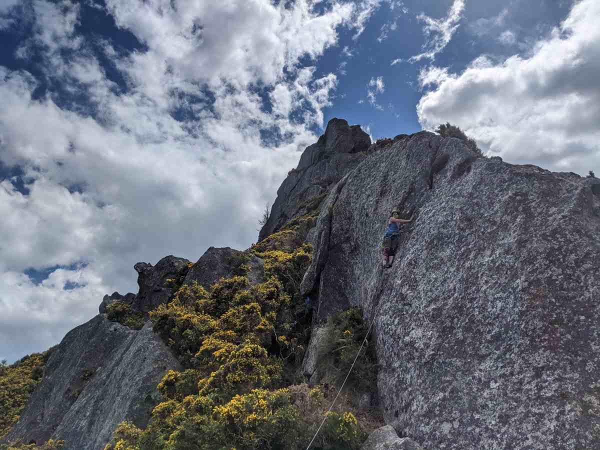 Climber on rock slab above bushy gully, below sharp skyline with dramatic clouds.