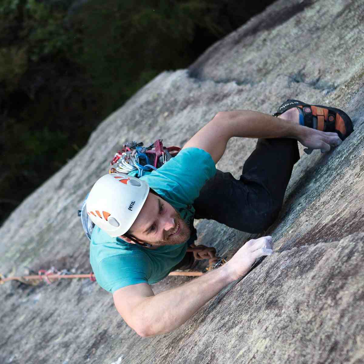 Climber in blue shirt and white helmet climbs a crack in a rock face, seen from above.