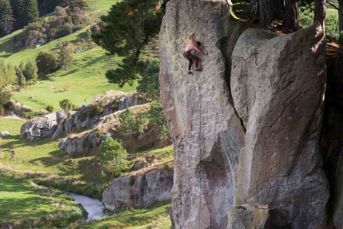 A climber on pocketed ignimbrite overlooking a stream and farmland.