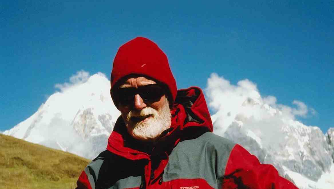 Sir Graeme Dingle in a red hat and sunglasses against a snowy mountain background in Peru.