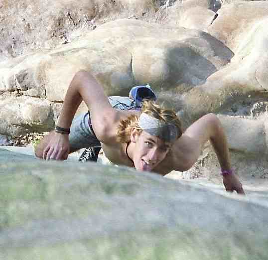 Young shirtless male climber in headband with chin close to rock seen from above