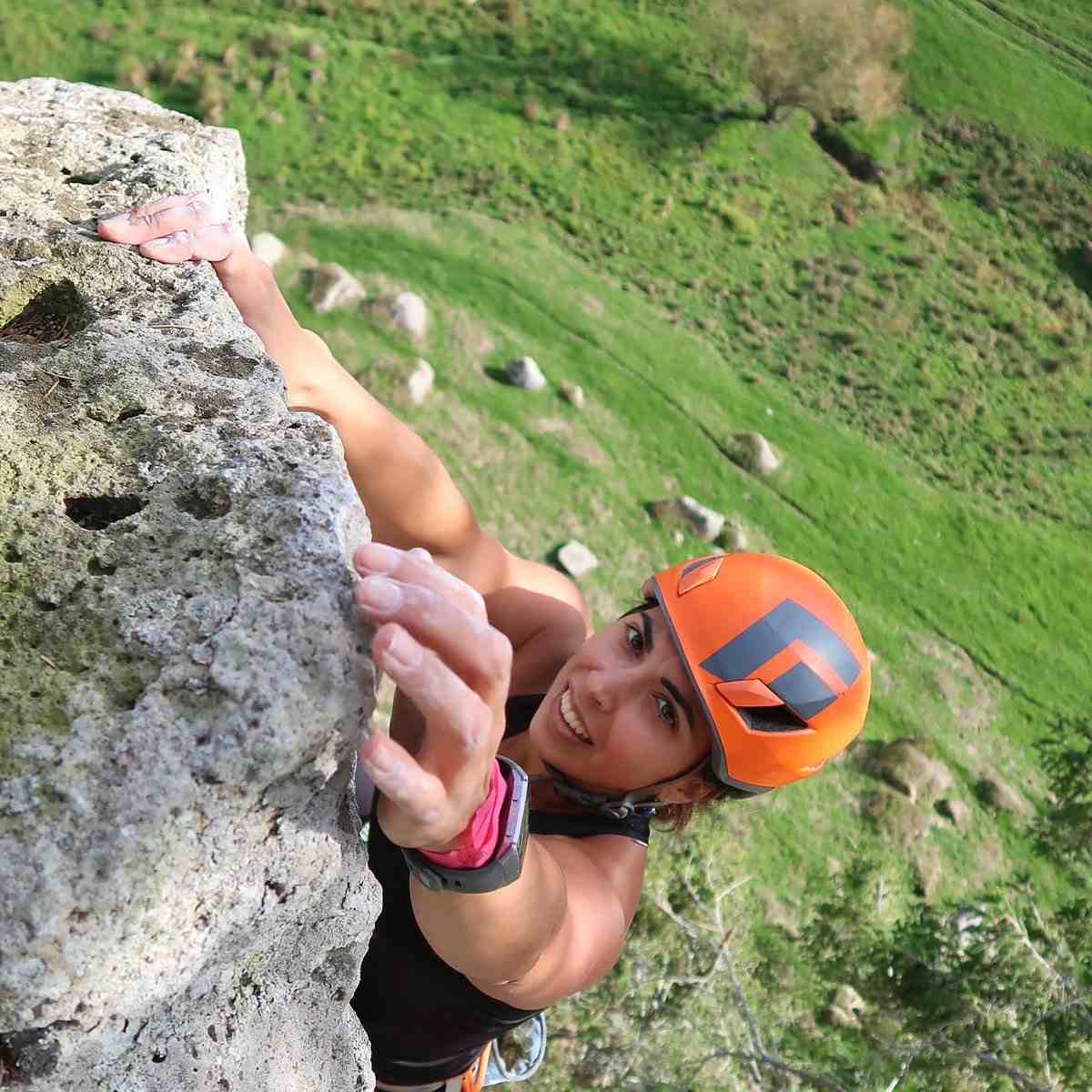 Female climber in orange helmet reaches for the final hold, viewed from above