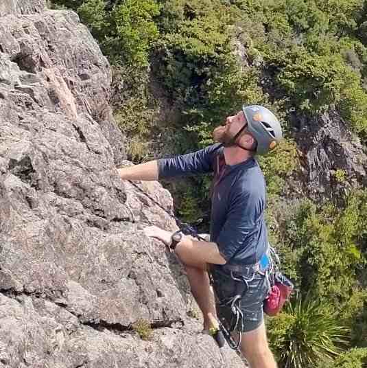 Bearded climber in blue shirt looking up against bush background
