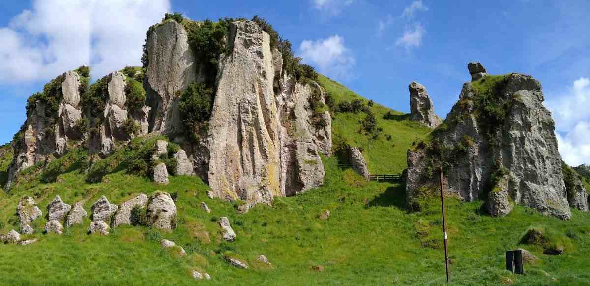 Sunlit rock buttresses rise from green farmland hills under a blue sky.