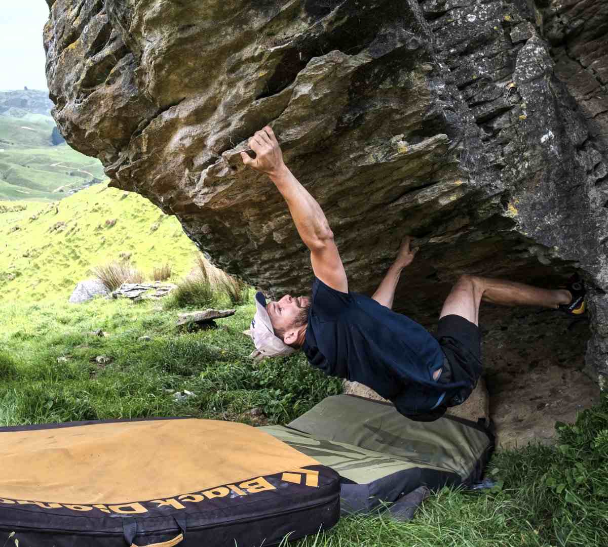 Boulderer in cap under steep limestone overhang at ground level with pads.