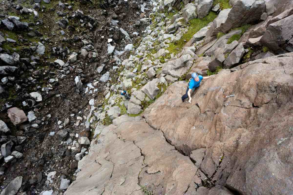 A climber in a blue helmet and shirt on a cracked alpine rock face, seen from above.