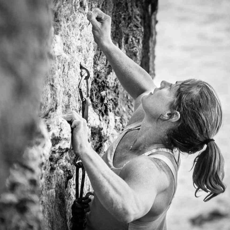 Female climber with ponytail looking up a rock face.