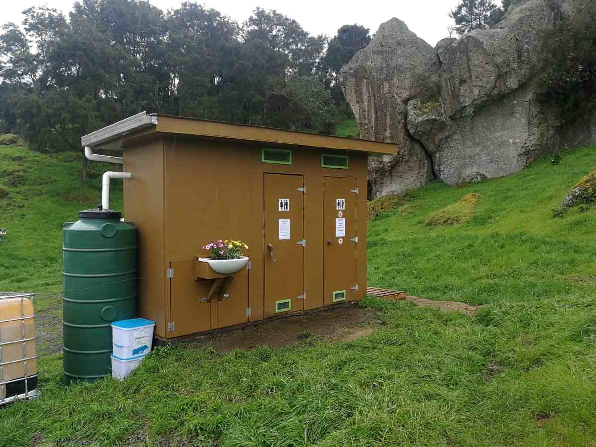 Brown Waipari toilet block with flowers in basin, in front of grass and cliffs