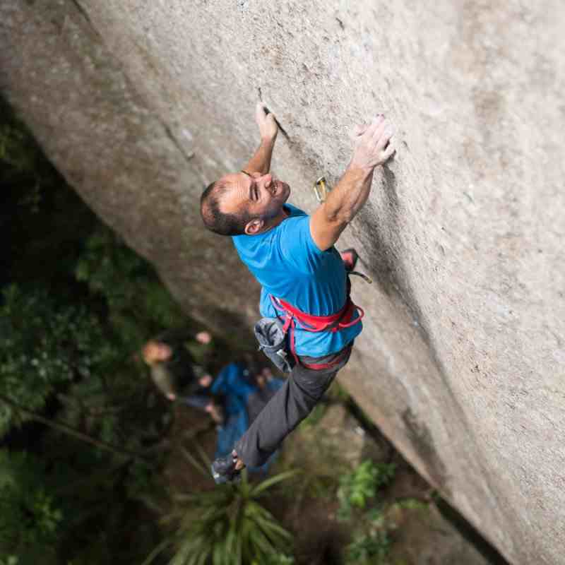 Climber in blue shirt makes a dynamic move on a smooth rock face.