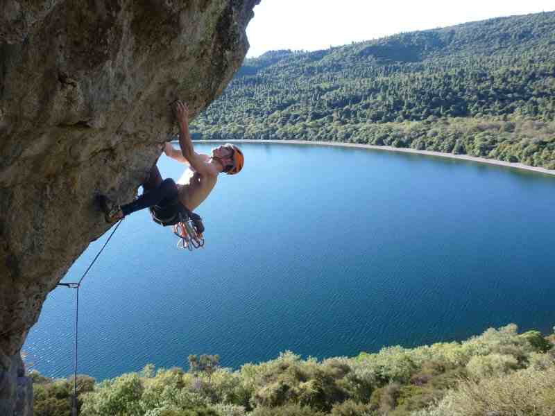 Climber on steeply overhanging rock with lake in the background.