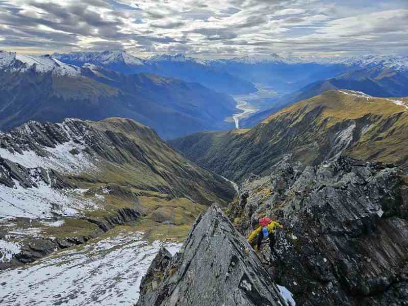 Climber in green scrambling in snowy mountains