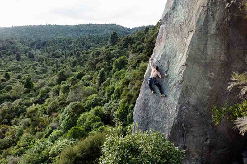Photo of climber on grey rock with forest below