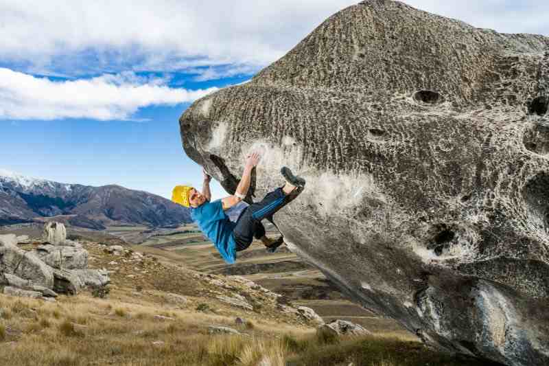 Climber on steep overhanging boulder with mountains in the background.